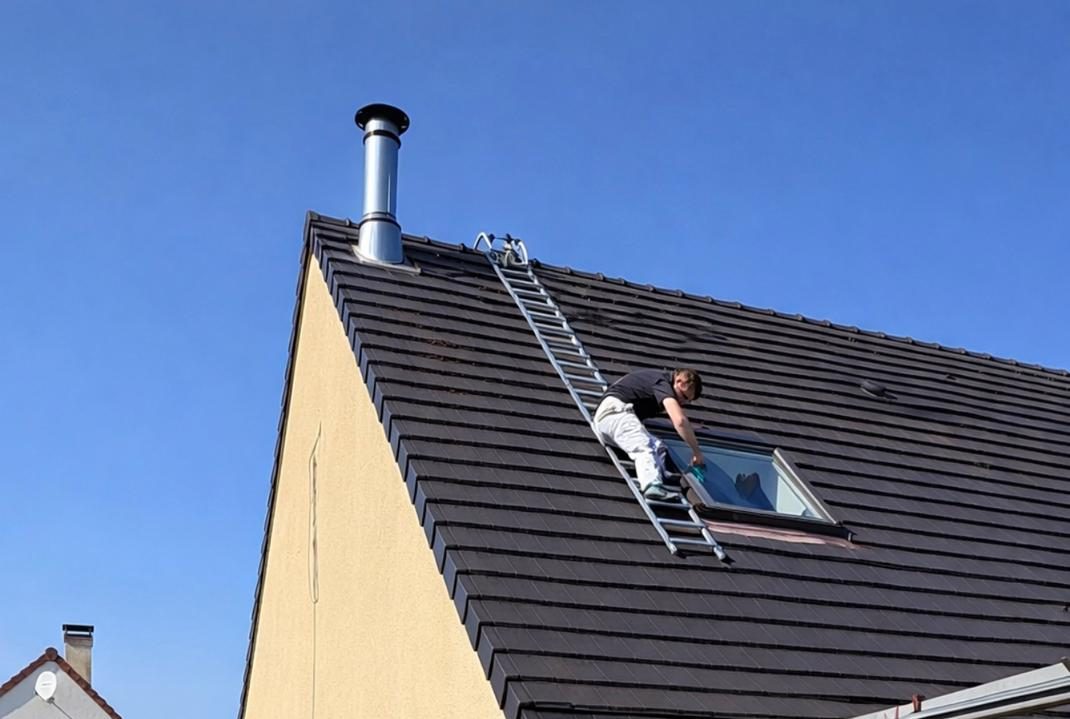 Couvreur de l'Entreprise Baud 41 nettoyant une fenêtre de toit sur une toiture en Loir-et-Cher